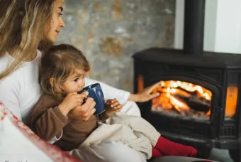 Femme avec un enfant sur ses genoux devant le poêle